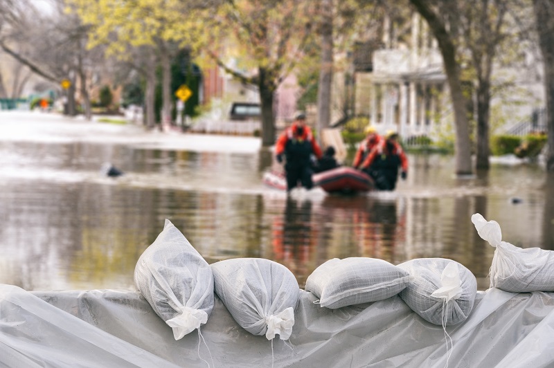 Sandbags holding back flood waters with two rescuers in the flood waters.