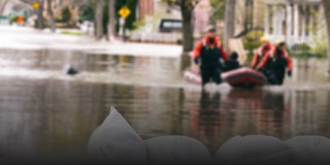 Sandbags holding back flood waters with two rescuers in the flood waters.